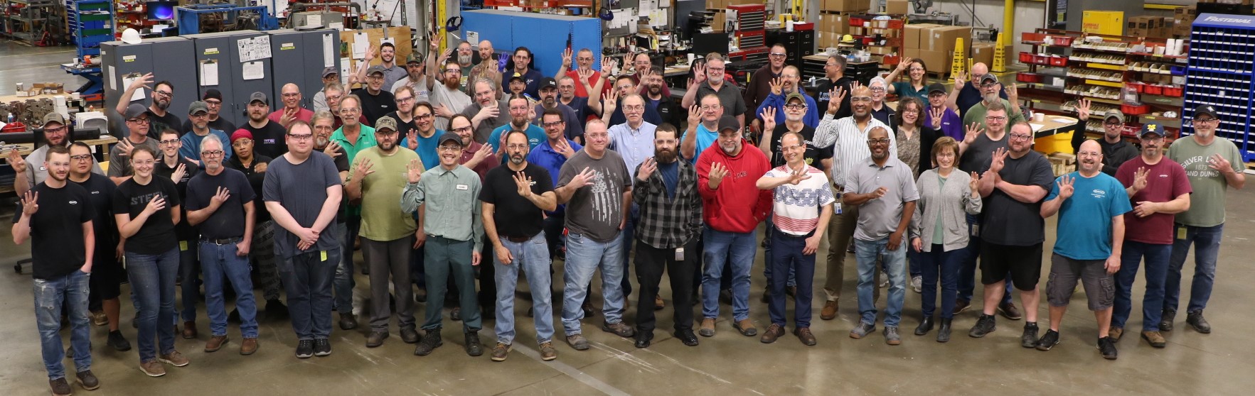 The image depicts workers from MTM in a group holding up four fingers to signify the number of years that have passed since their last recordable incident.