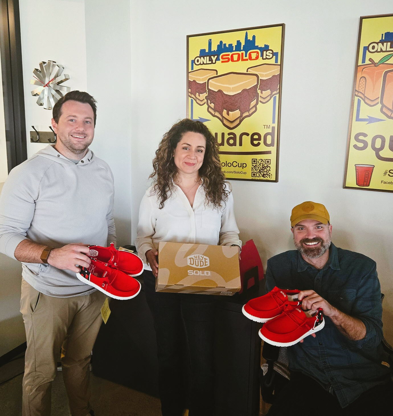 Three people holding two red pairs of shoes.